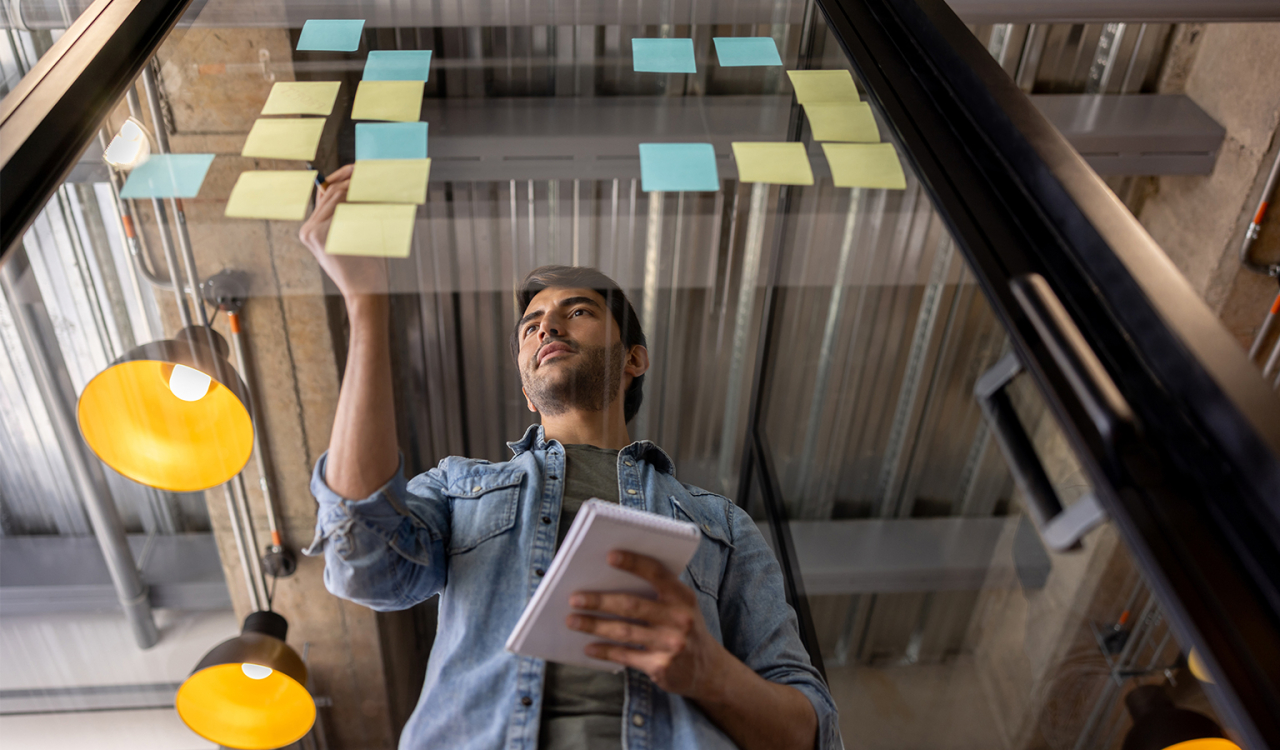 Image of man sticking post its on glass wall.